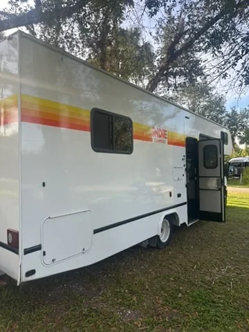 A white camper parked on grass beneath trees in Florida, with its side door open
